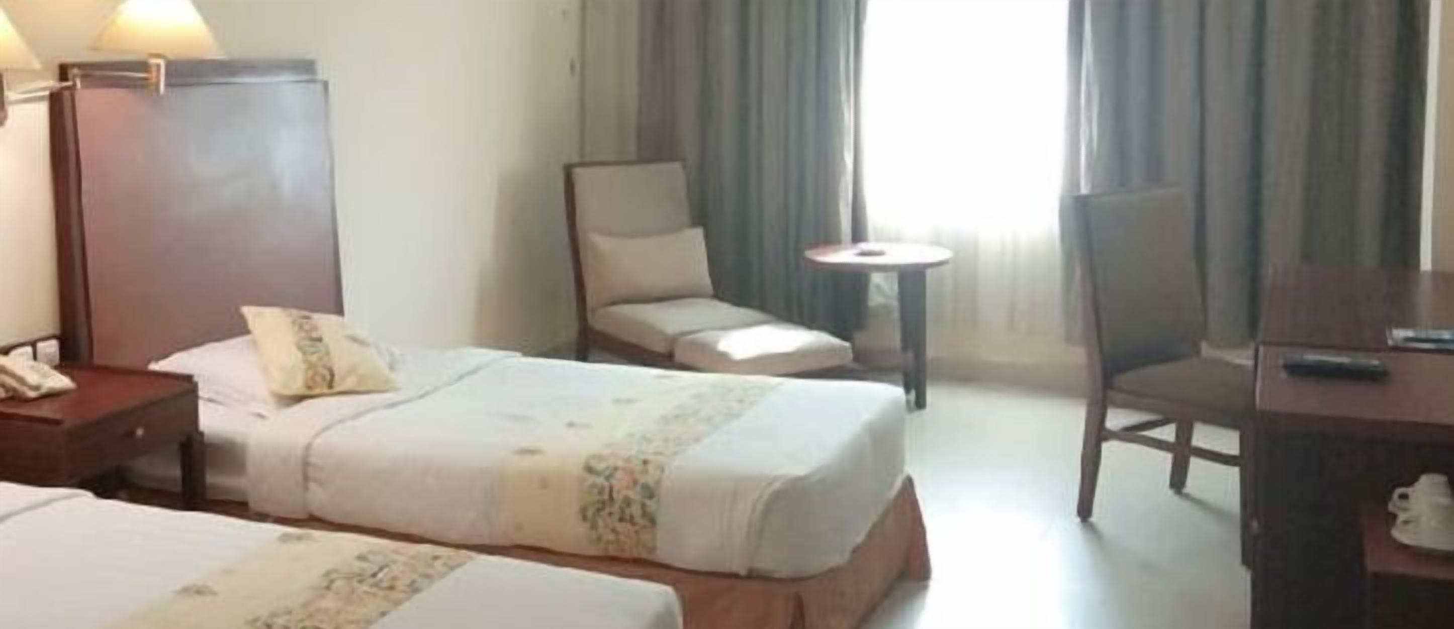 A hotel room with two beds, a chair, a small table, and a desk.
