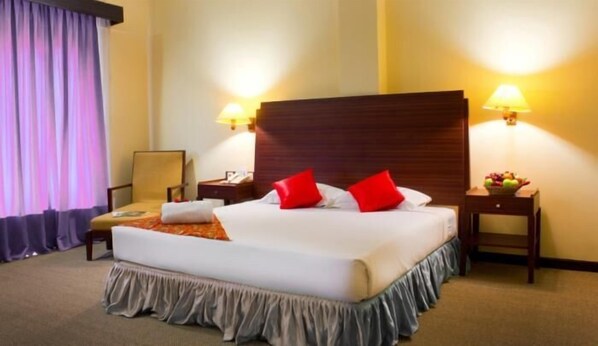 Habitación de hotel con una cama grande, dos mesitas de noche, una lámpara y un frutero.