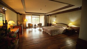 A spacious hotel room with a large bed, two bedside tables, a desk with a lamp, a chair, and a view of the outdoors through the window. - Angkham Hotel (Vientiane)