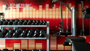 A gym with rows of dumbbells, weight machines, and a red wall with a logo. - Angkham Hotel (Vientiane)