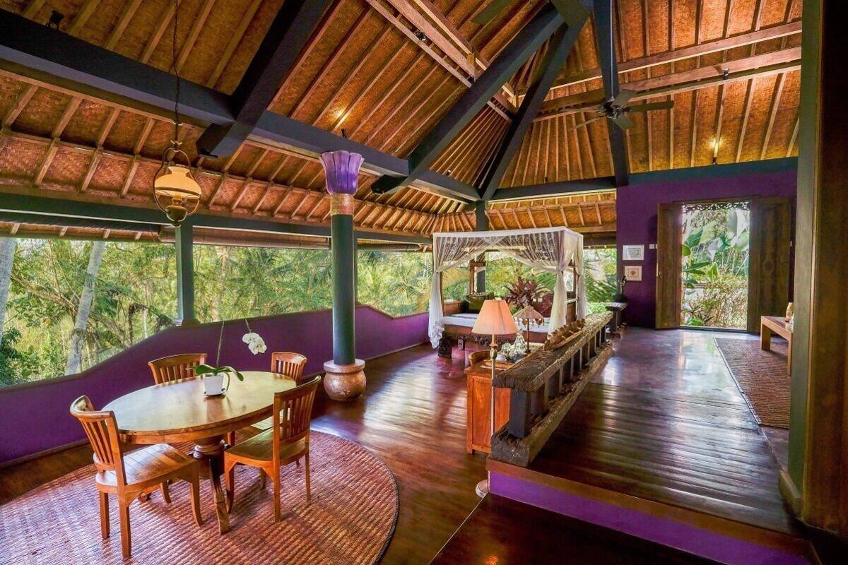 A spacious room with a wooden ceiling, a round dining table with chairs, a sofa, and a small table with a lamp.