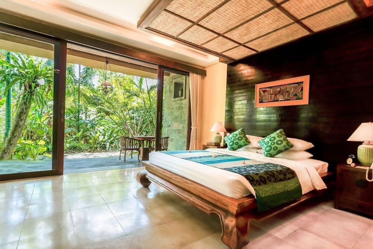 A spacious bedroom with a large bed, a view of lush greenery, and a sliding glass door leading to an outdoor area.