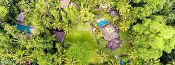 An aerial view of a resort with multiple swimming pools surrounded by lush greenery and palm trees.