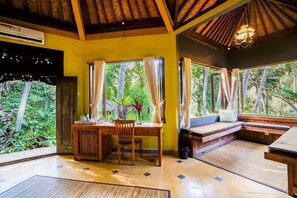 Una habitación con un escritorio de madera, una silla, un banco y ventanas amplias con cortinas.