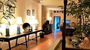 A well-lit hallway with a dining area, featuring a long table with lamps, a potted plant, and a decorative horse statue.