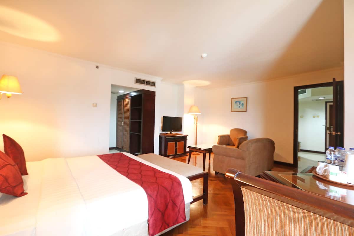 A hotel room with a bed, a chair, a desk, a television, and a door leading to another room.