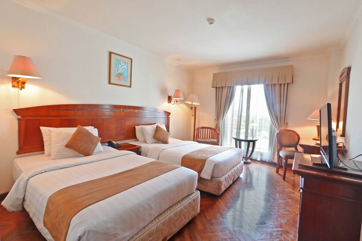A hotel room with two beds, a desk, a chair, and a television.