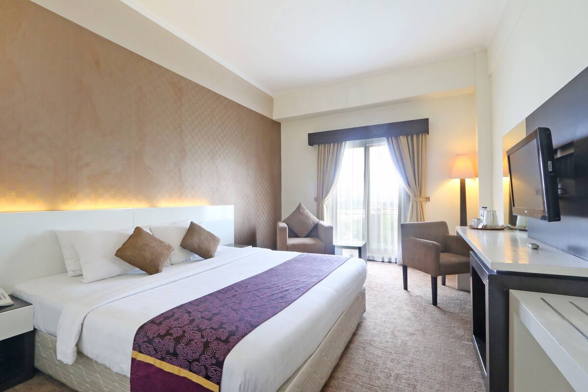 A hotel room with a large bed, a desk, a TV, and a chair.