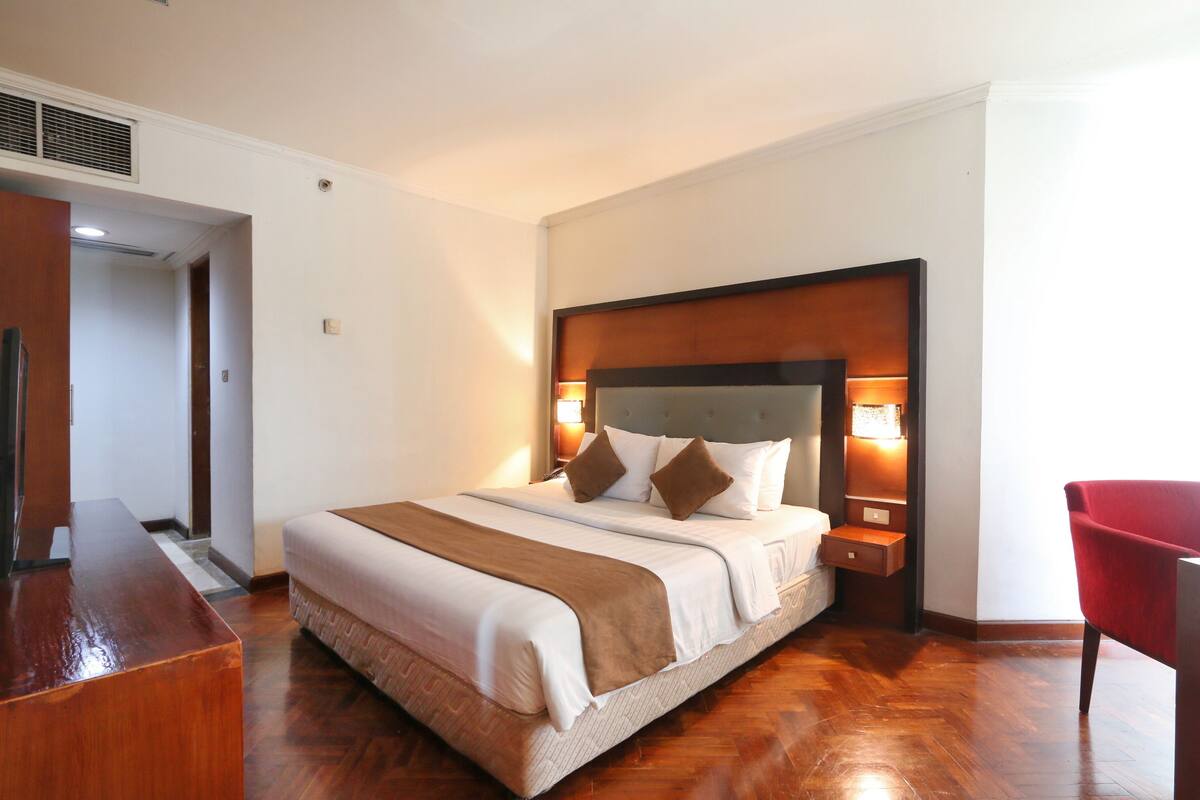 A neatly made bed with a wooden headboard, a bedside table, and a red chair.