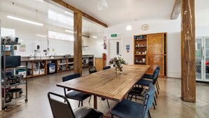 A spacious kitchen with a long wooden table, blue chairs, and various kitchen appliances. - Verandahs Parkside Lodge - Hostel (Auckland)