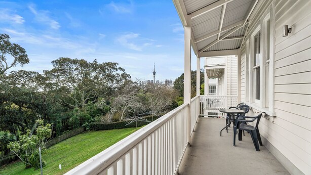 A covered balcony with a view of a city skyline, including a tall tower, and a well-maintained lawn. - Verandahs Parkside Lodge - Hostel (Auckland)