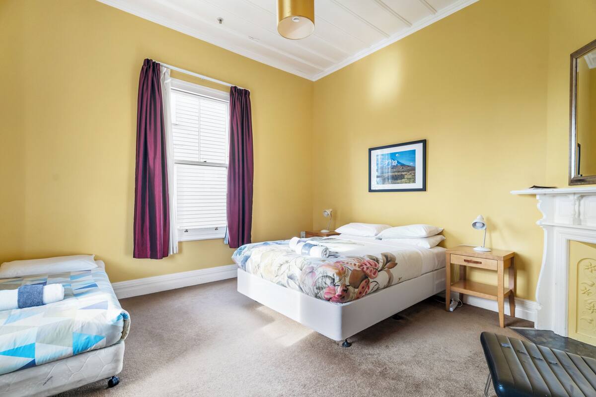 A bedroom with a bed, a bedside table, a chair, and a window with curtains.