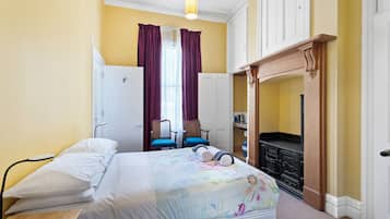 Un dormitorio con cama, escritorio, silla, armario y chimenea.