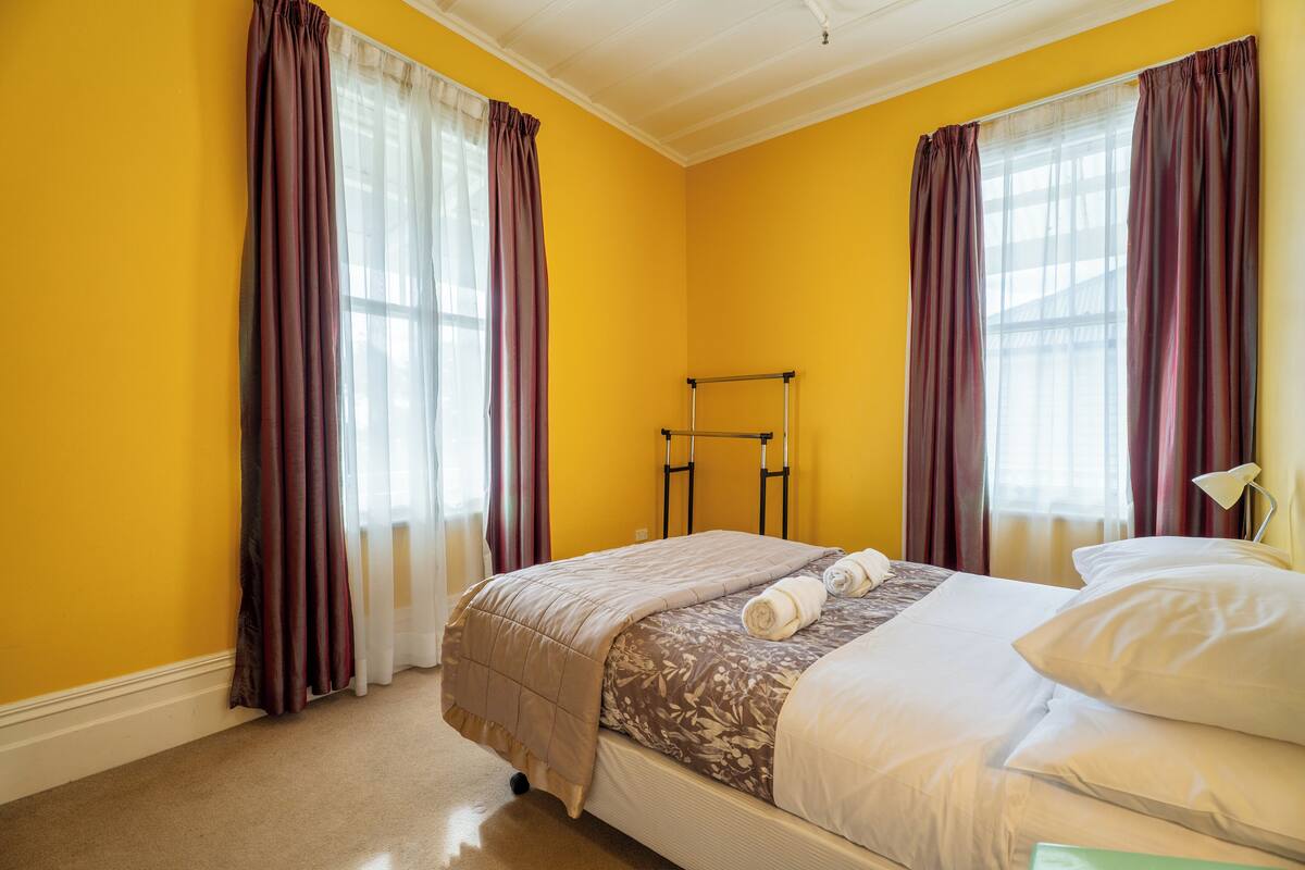 A hotel room with a bed, a window with curtains, a nightstand, and a lamp.