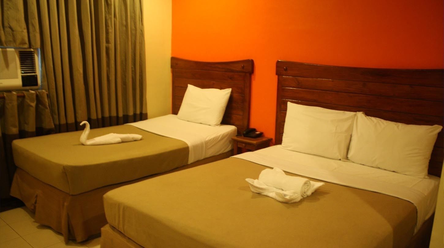 A hotel room with two single beds, each with a wooden headboard and white linens.