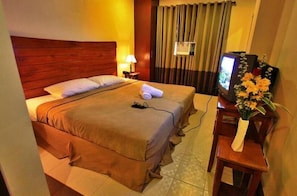 A hotel room with a large bed, a TV, a lamp, and a vase with flowers. - Staylite Hotel (Candon)