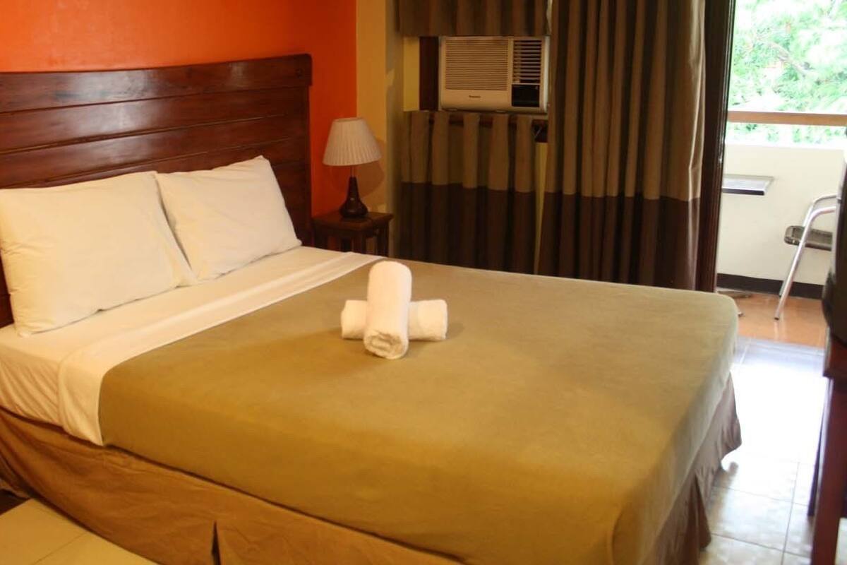 A neatly made bed with a brown headboard, a white pillow, and a rolled towel on the bed.