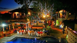 A poolside area with tables and chairs, a pool, and a building with string lights. - Staylite Hotel (Candon)