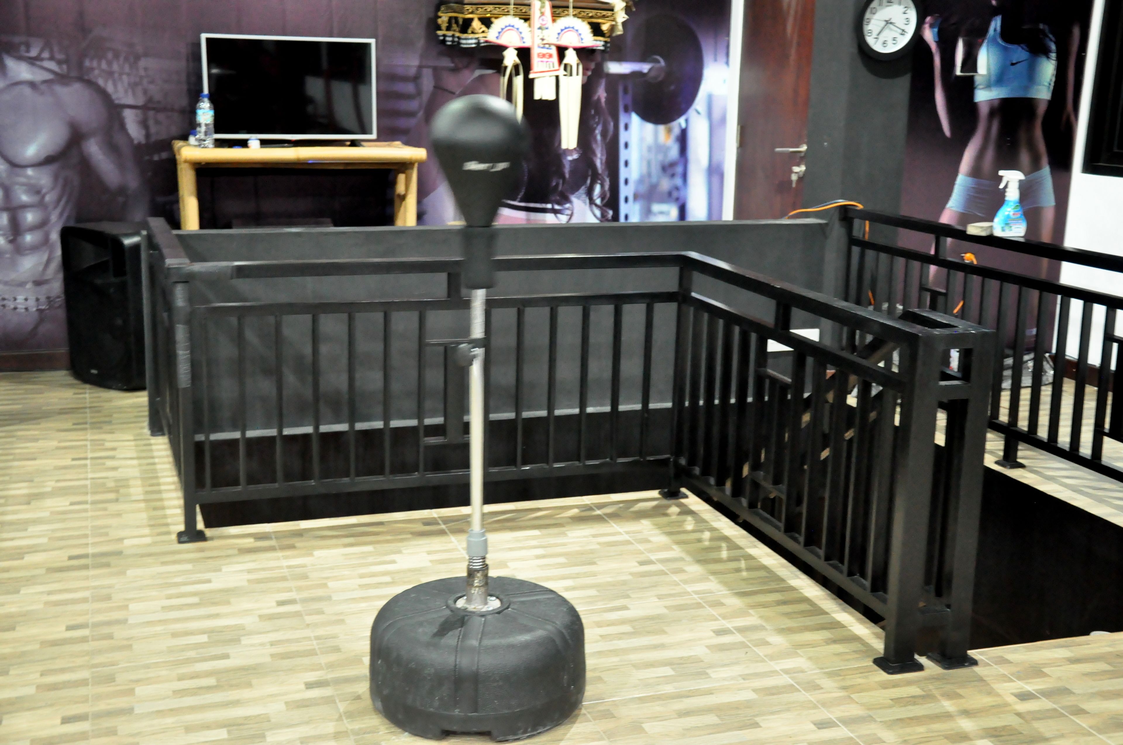 A corner of a room with a black metal railing, a black stool, and a wooden table with a television.