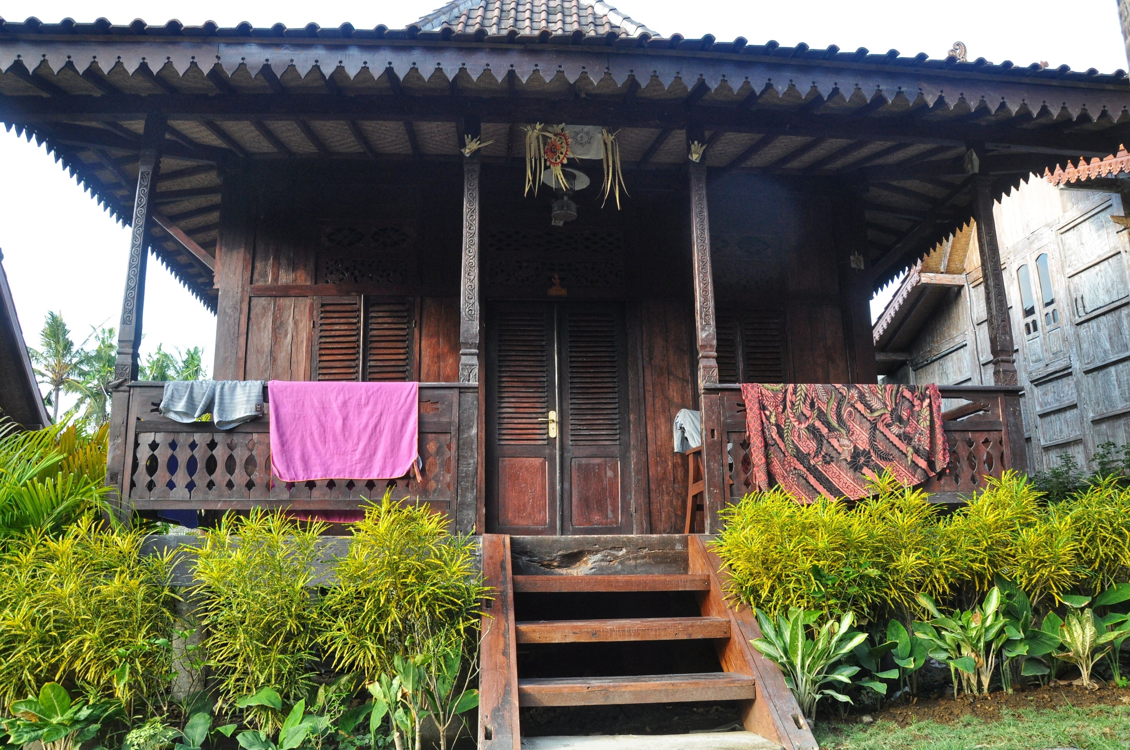 A traditional wooden house with a porch, steps leading to the entrance, and a door with a decorative hanging.