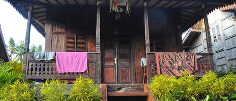 A traditional wooden house with a porch, steps leading to the entrance, and a door with a decorative hanging.