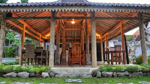 A traditional wooden pavilion with a tiled roof, surrounded by a garden with rocks and plants. - Kubudiuma Villas (Pererenan)