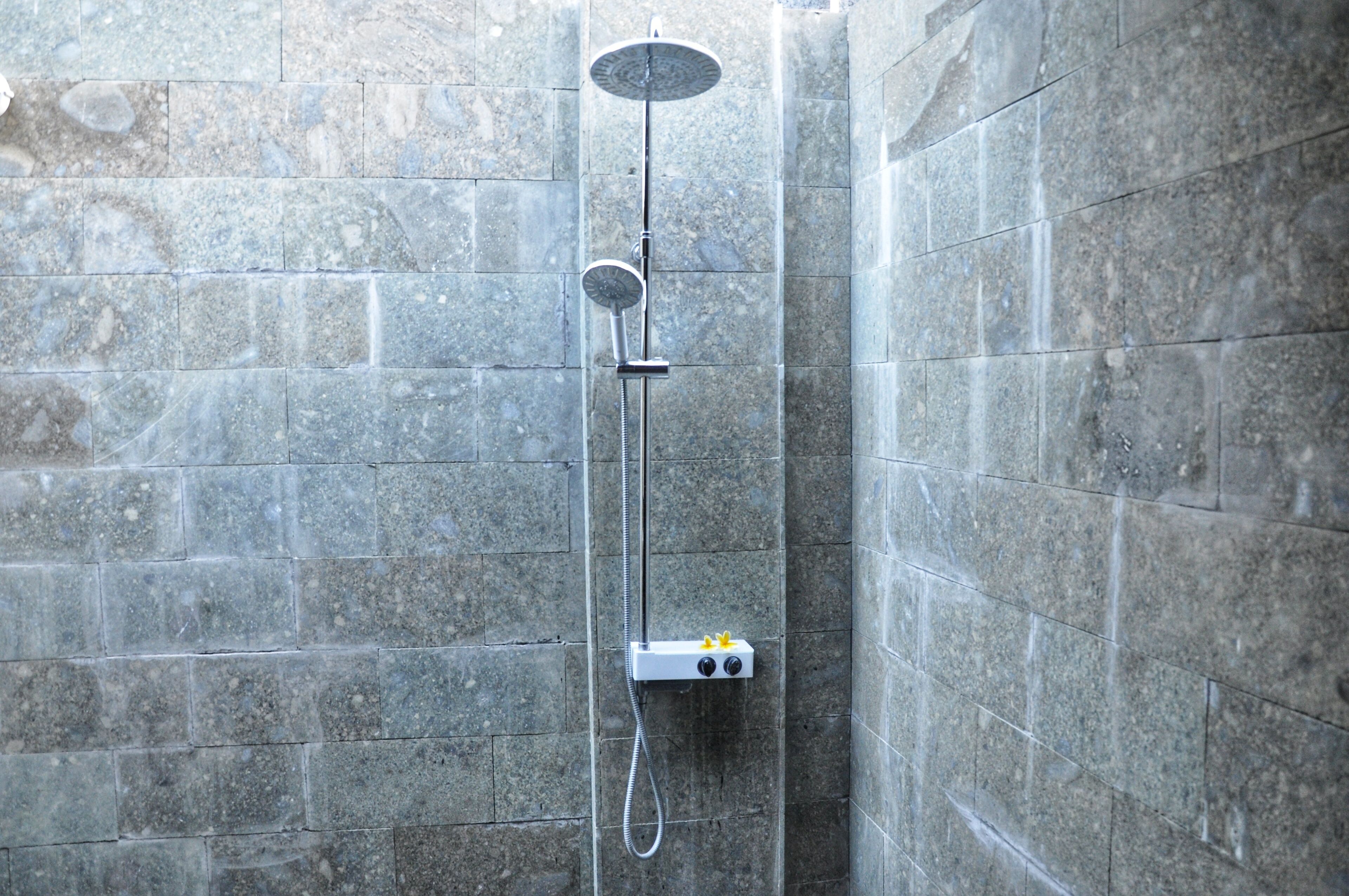 A shower with a handheld showerhead and a fixed showerhead, both mounted on a wall with a control panel.