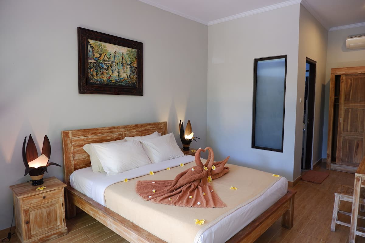 A neatly made bed with a towel art design, a bedside table with a lamp, and a painting on the wall.