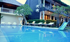 A swimming pool with lounge chairs and a slide, surrounded by greenery and a building with balconies. - Kubudiuma Villas (Pererenan)