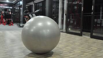 Una gran pelota de ejercicios gris en un gimnasio, con equipo de ejercicio y un cartel que dice 'PERS COMPLAINT'.
