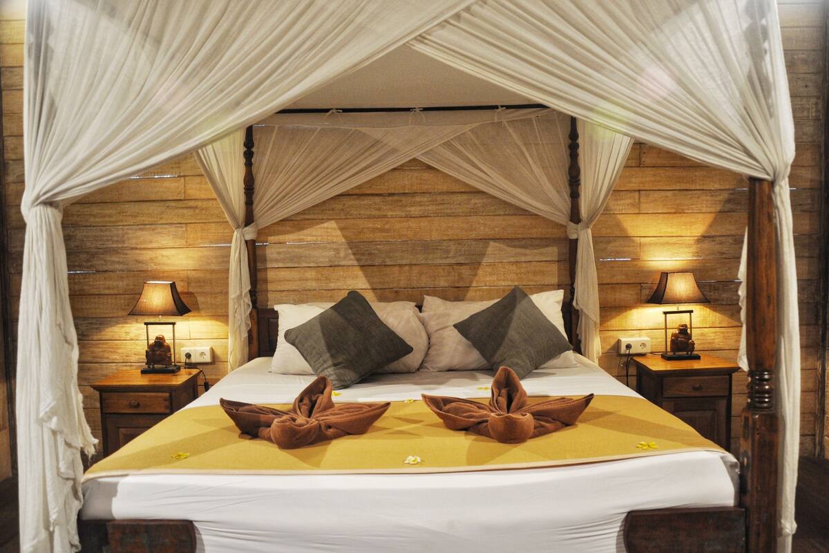 A bed with a canopy, two bedside lamps, and a wooden headboard.