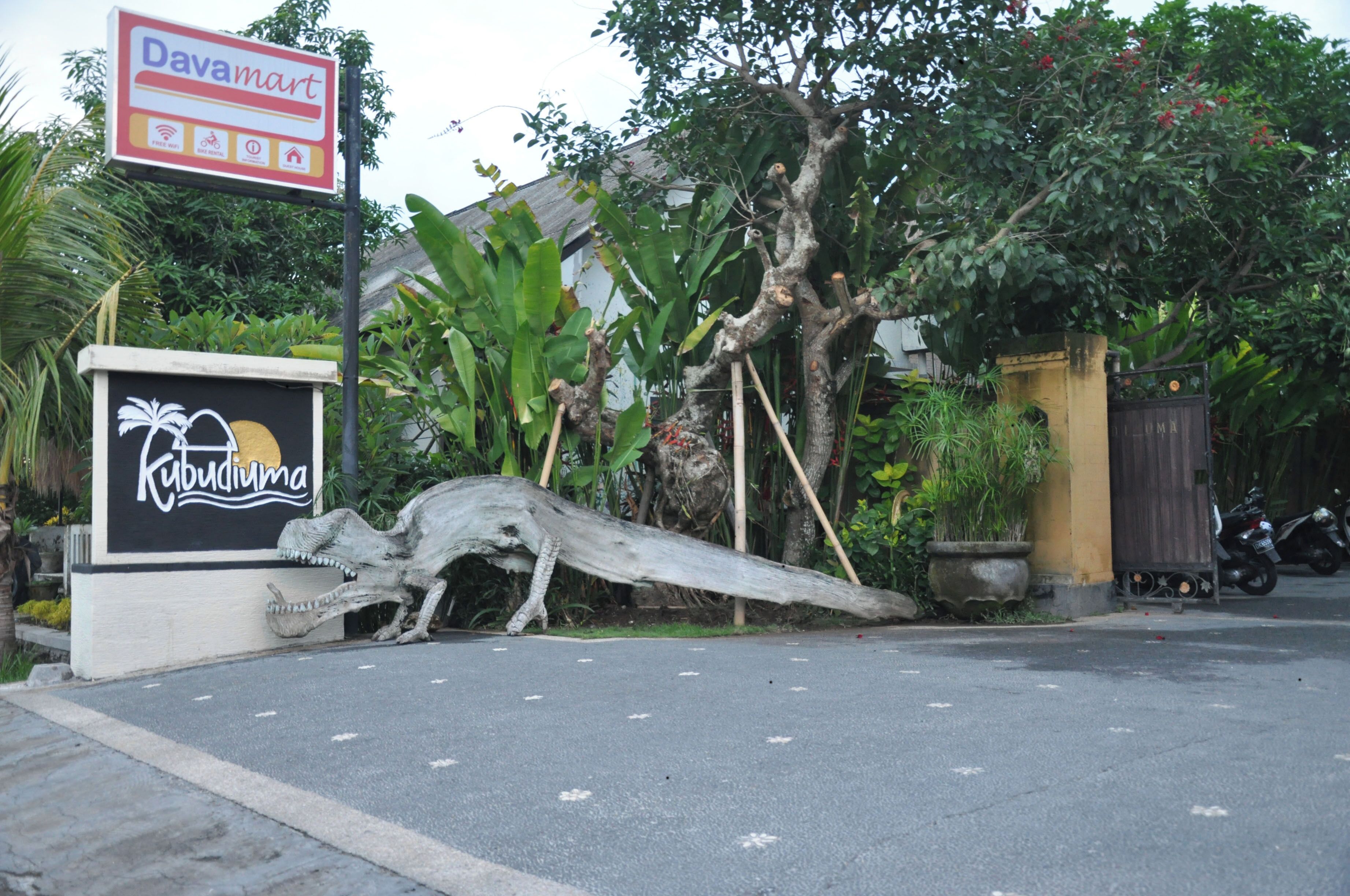 A sign for Davamart and Kubudima, with a large tree and a motorcycle parked nearby.