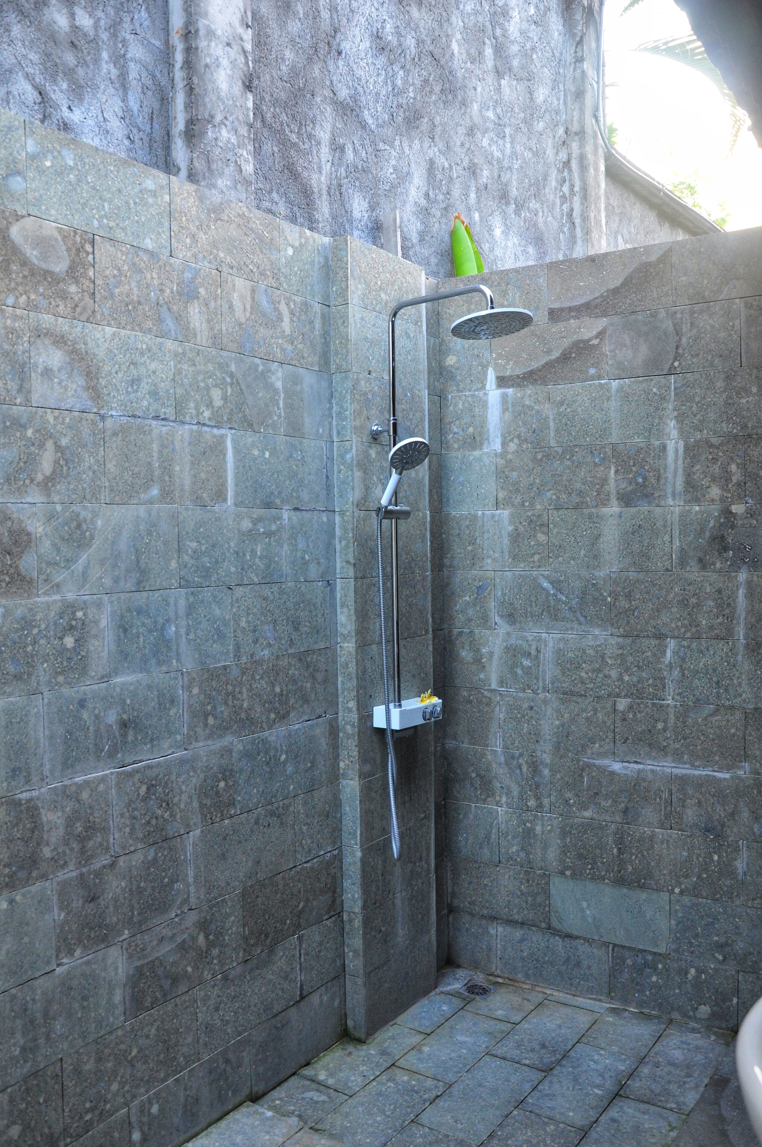 A stone-walled shower enclosure with a handheld showerhead and a rain showerhead.