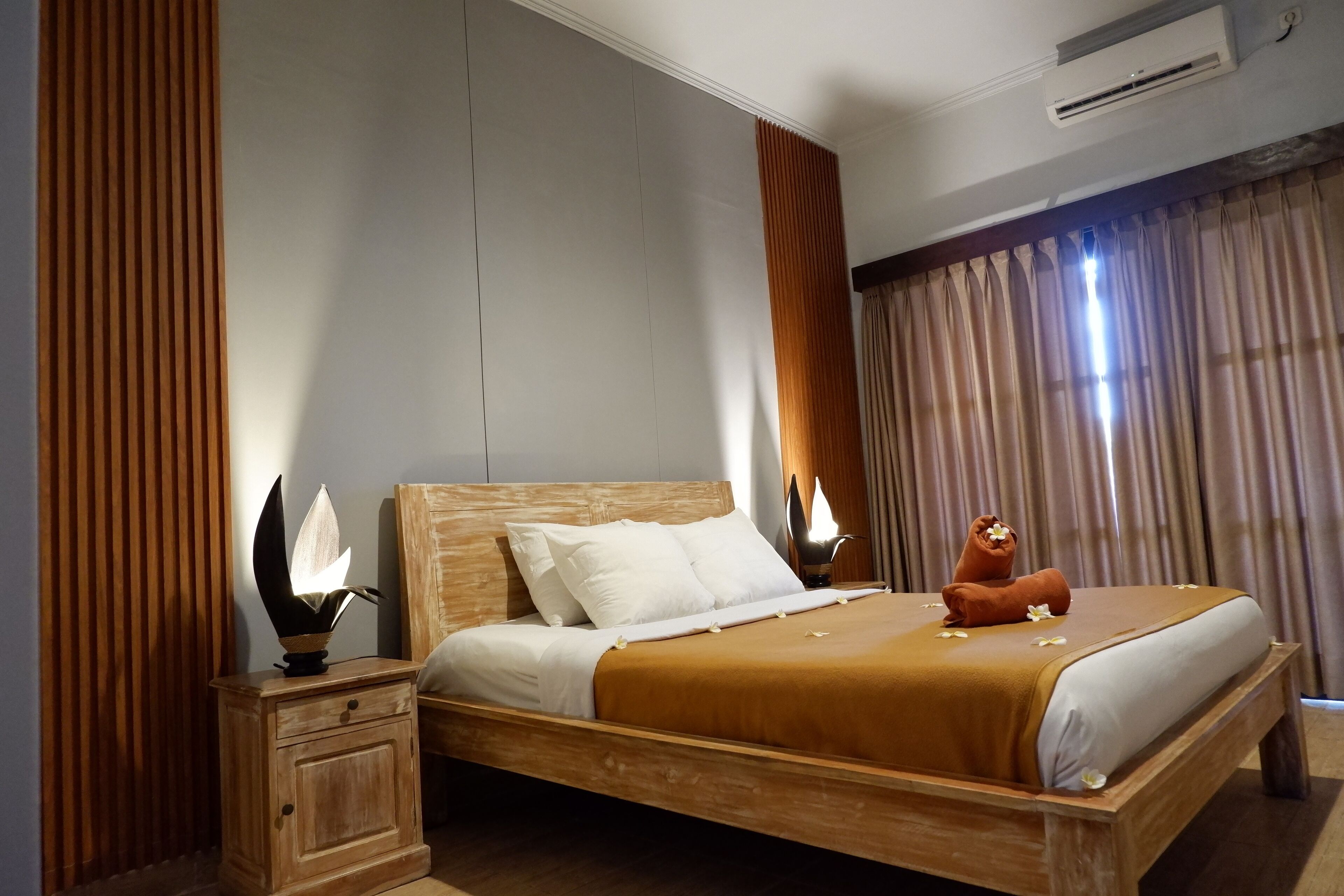 A neatly made bed with a wooden headboard, a bedside table with a lamp, and a window with curtains.