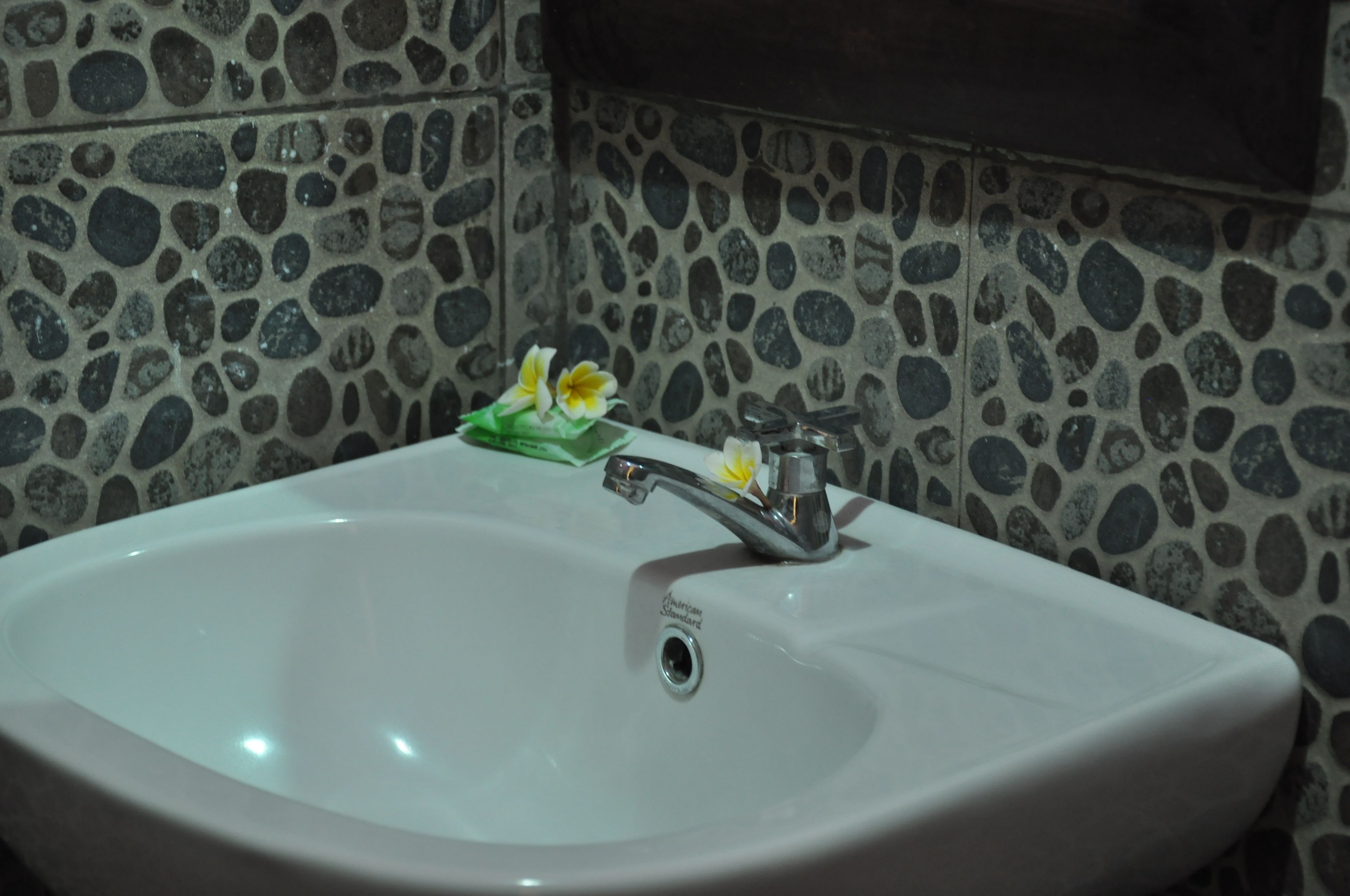 A bathroom sink with a modern faucet, a flower arrangement, and a stone-patterned wall.