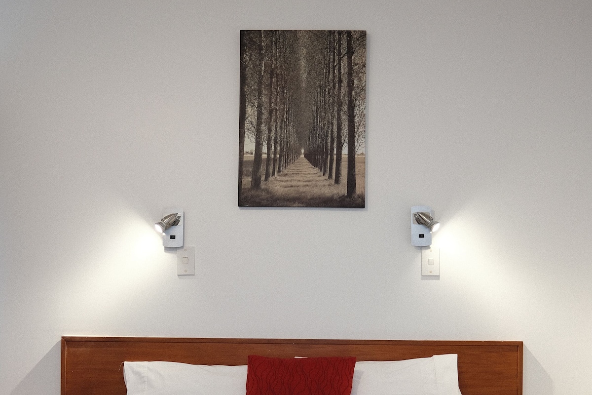 Une chambre à coucher avec un grand lit, une tête de lit en bois, deux tables de chevet et un luminaire fixé au mur.
