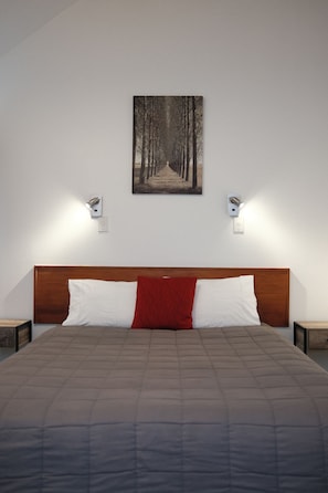 A bedroom with a large bed, a wooden headboard, two bedside tables, and a wall-mounted light fixture.