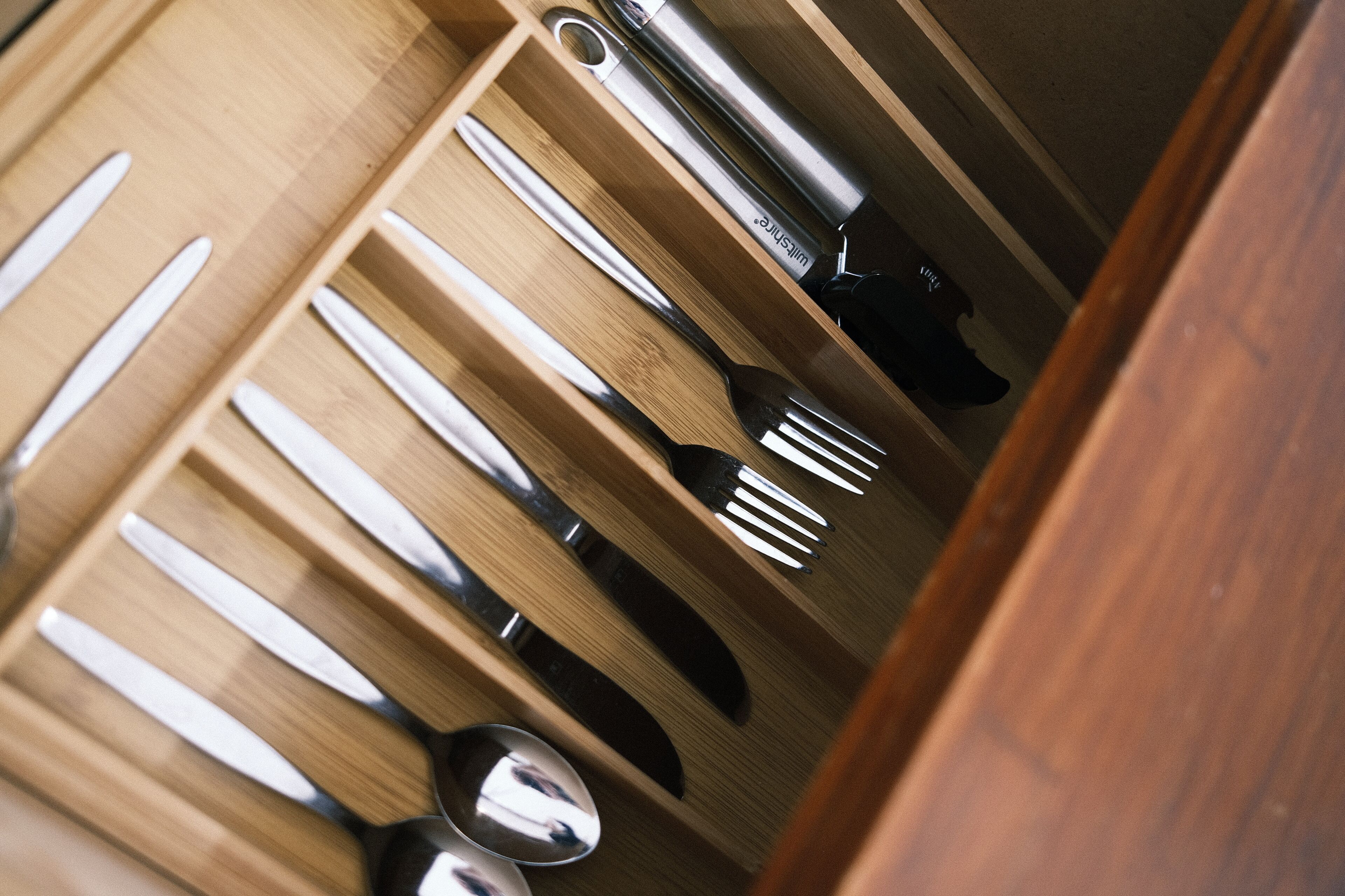 Eine Schublade mit ordentlich verstauten Küchenutensilien, darunter Messer, Löffel und eine Gabel.