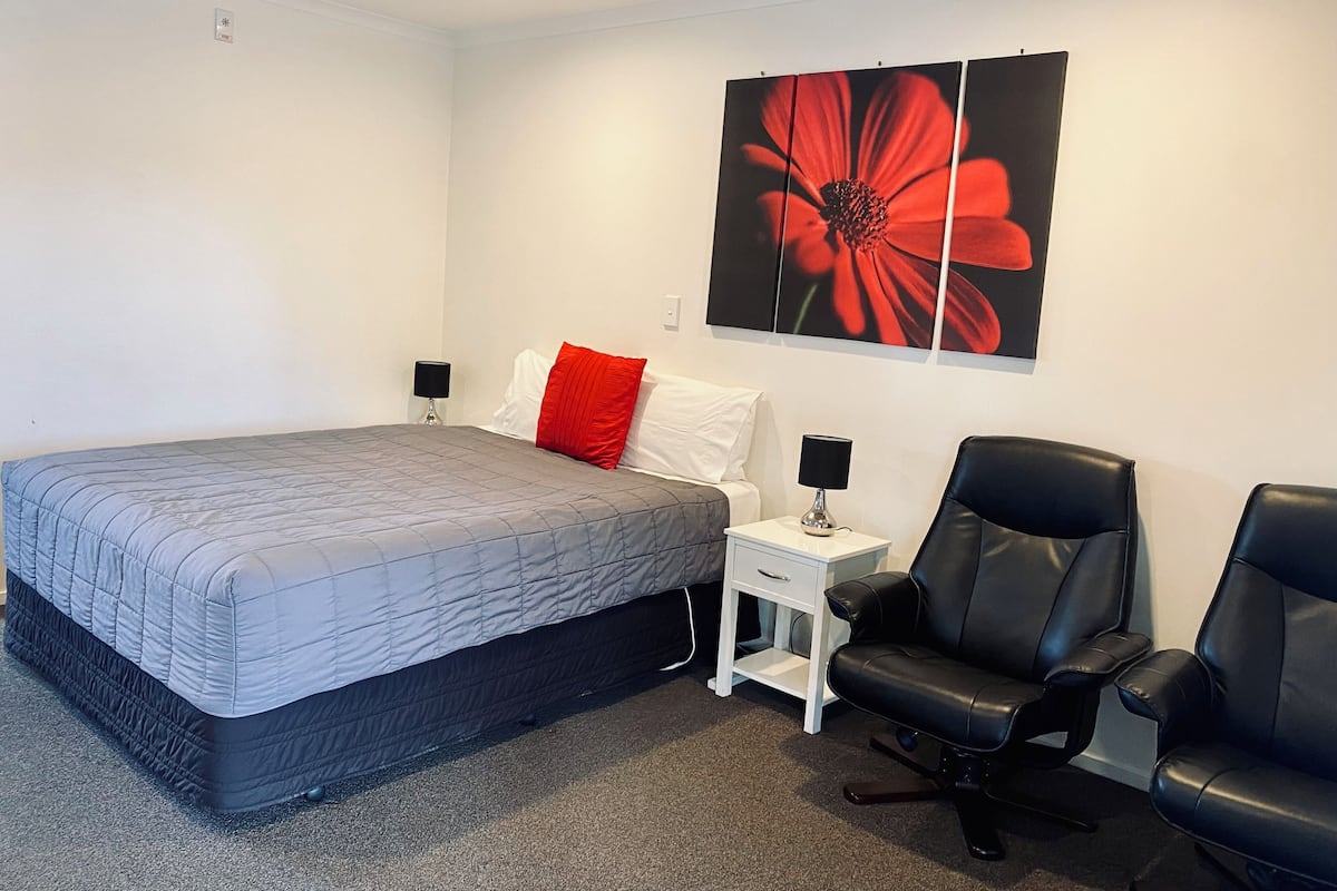 Une chambre à coucher comprenant un lit, deux tables de chevet avec des lampes, une chaise et une grande œuvre d’art à motifs floraux accrochée au mur.