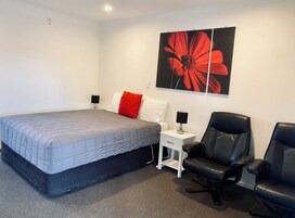 Un dormitorio con una cama, dos mesitas de noche con lámparas, una silla y una obra de arte floral de gran tamaño en la pared.