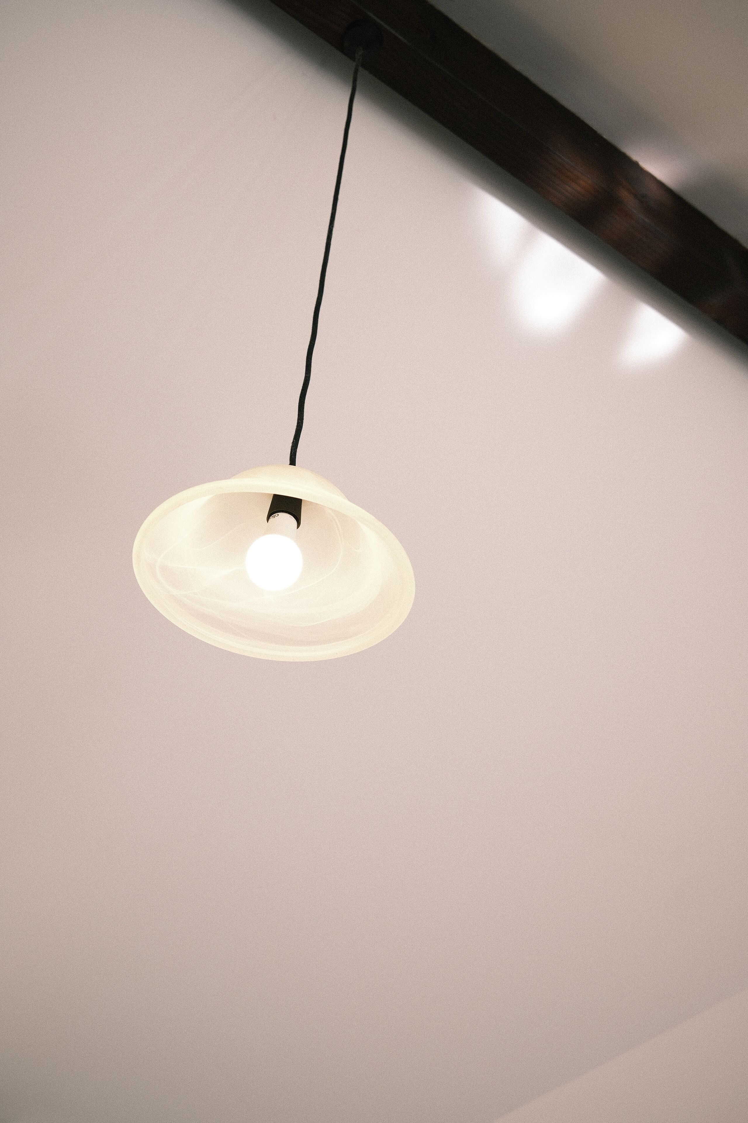 Una lámpara colgante con pantalla blanca y cable negro.