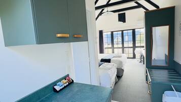 A modern kitchen with a stainless steel sink, green cabinets, and a view into a bedroom with a bed and a window.