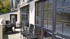 A modern building with large sliding glass doors, a patio area with outdoor furniture, and a view of the surrounding landscape. - Salty Dog Inn (Snells Beach)