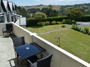 A balcony with a table and chairs, overlooking a well-maintained lawn and distant hills.