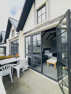 A hotel room with a sliding glass door, a bed, a small table, and a chair.