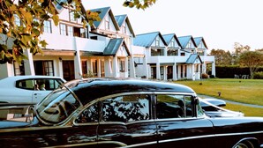 A classic black car parked in front of a modern white house with multiple levels and blue roofs. - Salty Dog Inn (Snells Beach)
