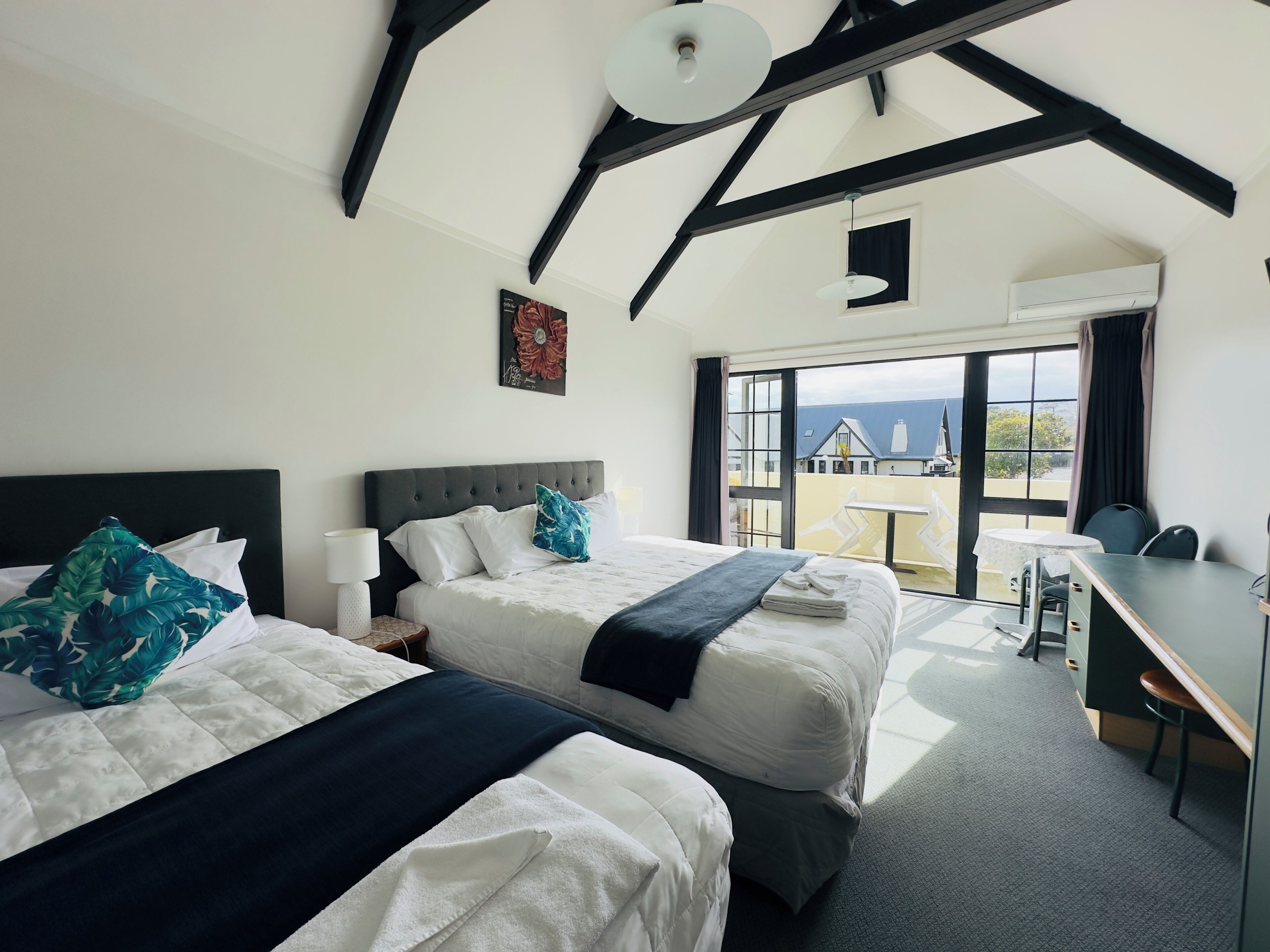 A hotel room with two beds, a desk, and a view of the sea.