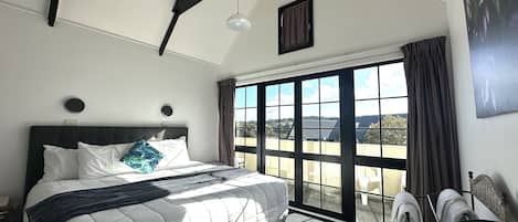 A hotel room with a large bed, a ceiling fan, a window with curtains, and a view of the outside.