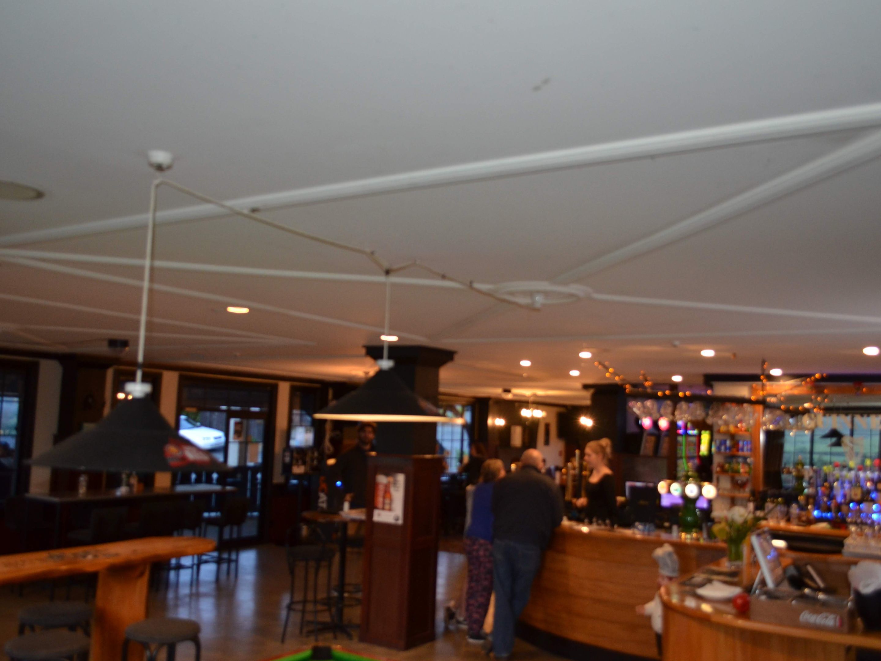 A bar area with a counter, stools, hanging lamps, and a bar stocked with bottles.
