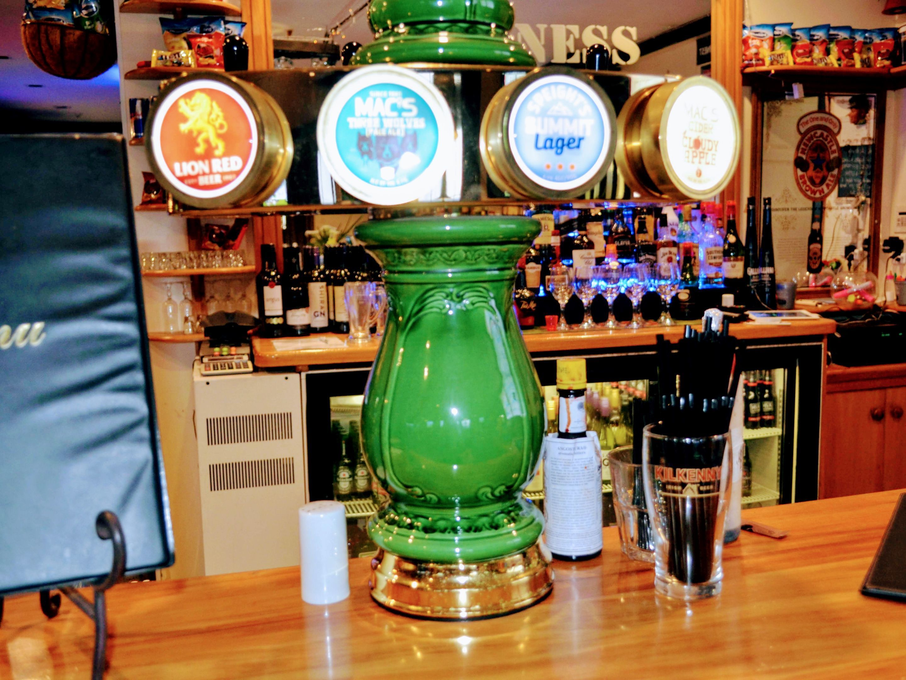 A bar area with a green decorative piece, a cash register, and various bottles and glasses on shelves.